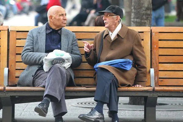 Dos hombres mayores conversan sentados en una banca