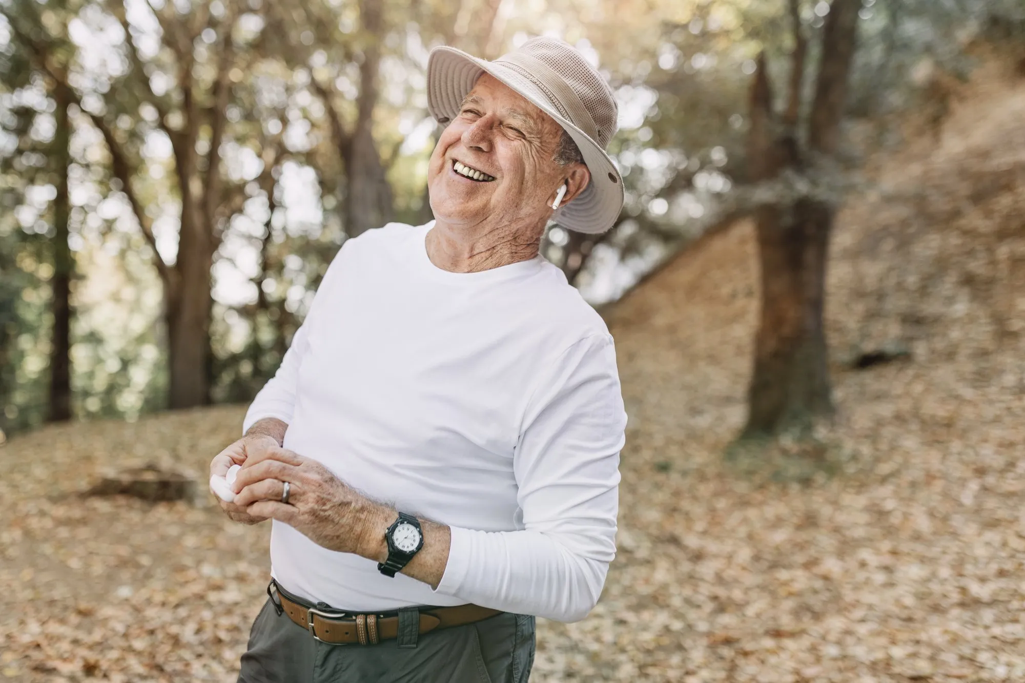 Hombre mayor sonriendo mientras escucha música en un bosque